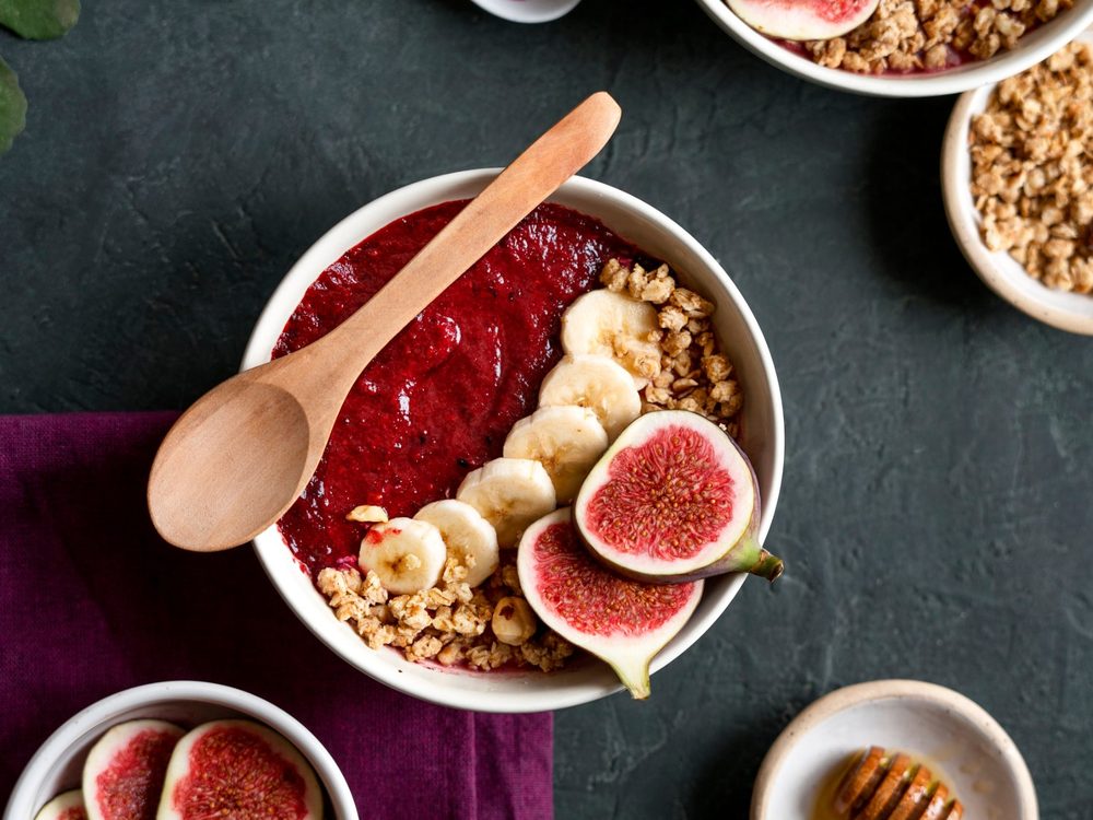 Bowl de açaí con higos, plátano y granola servido con cuchara de madera