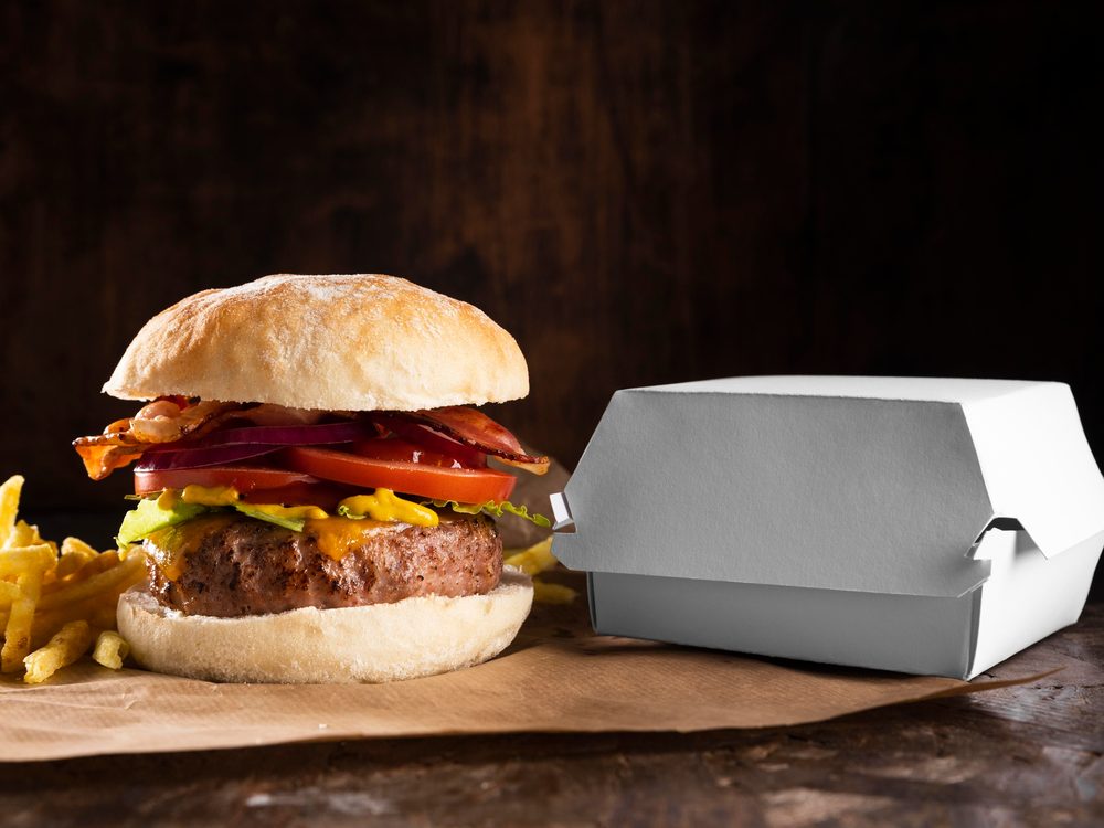 Hamburguesa con papas fritas junto a una caja de cartón blanca para llevar